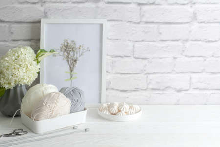 Yarn of light neutral shades in a white basket. Wall of old brick. Gray vase in the Scandinavian...