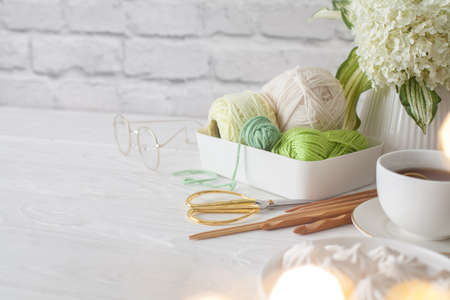 Green yarn in a white plastic basket. Knitting needles and scissors. Tea in a cup and biz. Aged...