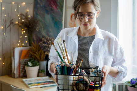 Girl artist illustrator holds a basket with paints, brushes and pencils.の写真素材