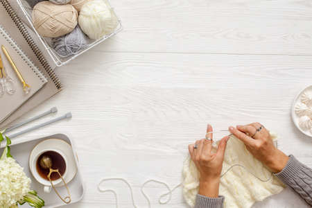 Female hands knitting with white wool, on a wooden background, top view. Handicraft accessories, tea, diary and hydrangea flowers.の写真素材