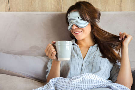Good morning! Woman woke up in bed. Woman drinking coffee in bed. Gray bedding. Eye patch.の写真素材