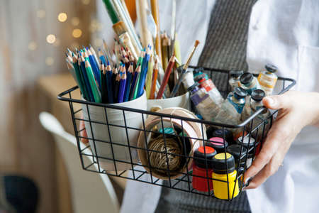 Girl artist illustrator holds a basket with paints, brushes and pencils.の写真素材