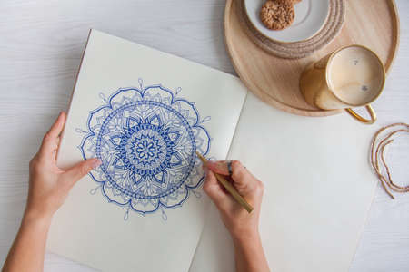 Female hands close up draw Decorative round floral mandala. Hobby and home relaxation. A mug of...