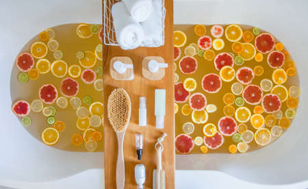Bathtub with mixed slices of fresh citrus fruits and spa set of natural product.