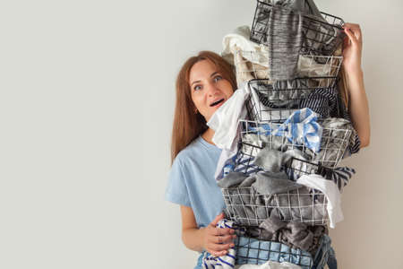 Surprised woman holding metal laundry basket with messy clothes on white background.の写真素材