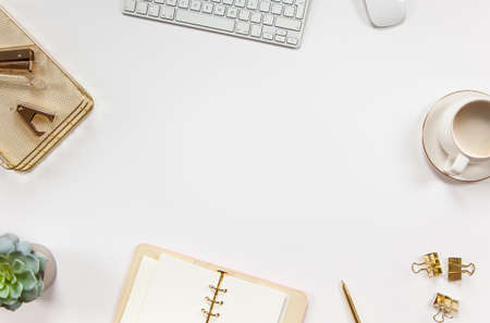 Office stationery supplies with keyboard, mouse, coffee and flowers placed in a circle on white deskの写真素材