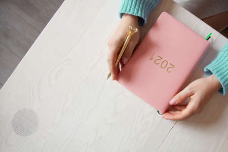 Woman sitting in knitted warm sweater with coral coloured 2021 diary on tableの写真素材