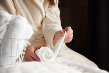 Woman in beige warm robe is folding the clean white hand towels and putting into a metal mesh basketの写真素材