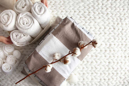 Woman hand holding a cotton branch with stack of folded linens near rolled up towels in mesh basketの写真素材