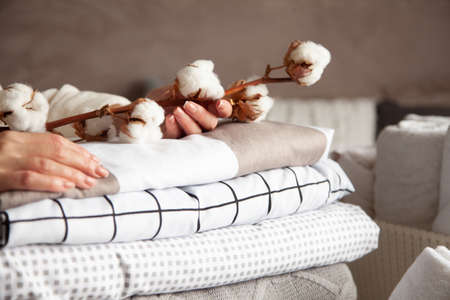 Well groomed woman hands holding the cotton branch with pile of folded bed sheets and blanketsの写真素材
