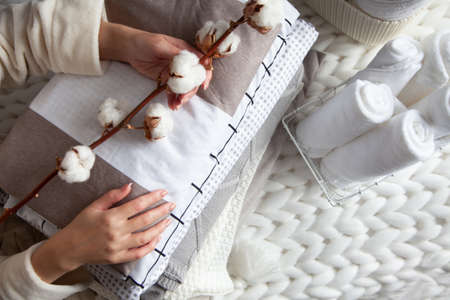 Woman hand holding a cotton branch with stack of folded linens near rolled up towels in mesh basket