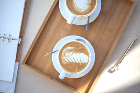 Top view two cups of coffee latte art foam is holding by woman hand with unfocused placed eyeglasses...
