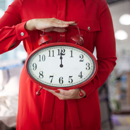 Woman in red dress holding with hands a huge clock showing 12 midnight of New Years Eve