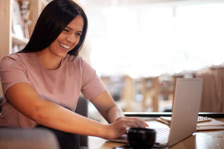 Concentrated young woman typing on computer while having a coffee break at her office interior.の写真素材