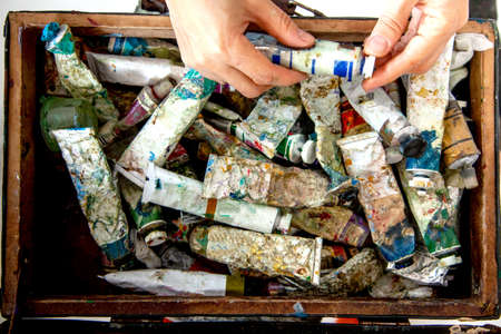 Painter hands picking oil paint tube from collection of neglected and messy artist oil paint tubesの写真素材