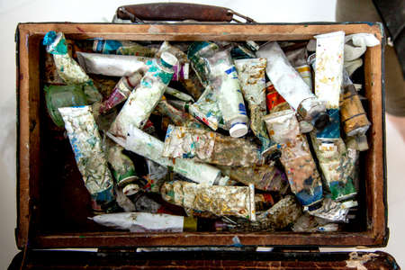 Painter hands picking oil paint tube from collection of neglected and messy artist oil paint tubesの写真素材