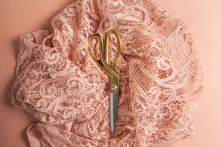 Flat lay of tailoring scissors placed on top of wrinkled coral color lace fabric with patternsの写真素材