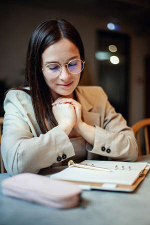Beautiful young woman in suit writing her business plans while drinking coffee on break timeの写真素材