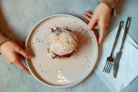 Woman hands holding plate of vegetarian burger with beetroot, lentil and red cabbage on bunの写真素材