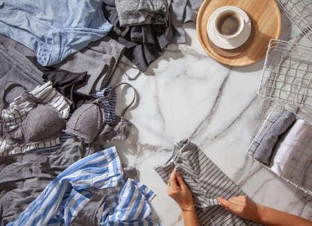 Woman hands is folding clothes and organizing stuff in white metal mesh basket on white marble...
