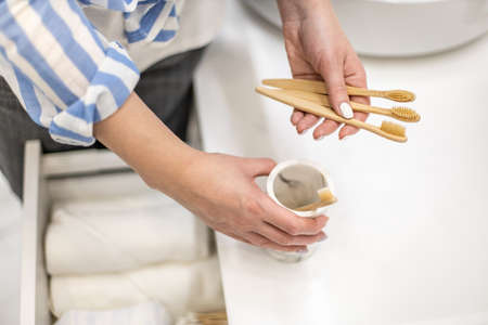 Woman organizing environmental bathroom amenities in drawer and putting bamboo toothbrush into a cup