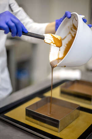 Smiling female confectioner pouring chocolate gommage on biscuit cake assembling mousse dessertの写真素材