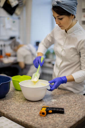 Woman confectioner in uniform pouring liquid matcha tea chocolate on table from bowl at cuisineの写真素材