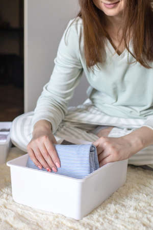 Laughing domestic woman rolled up clothes use Marie Kondos method. Placing apparel in cupboardの写真素材