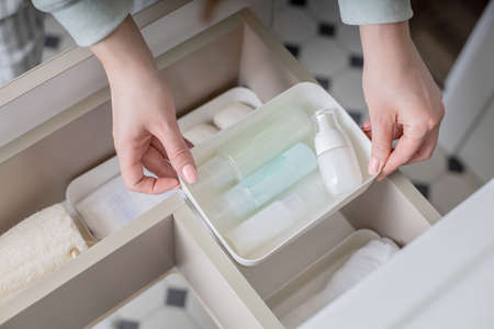 Top view female housewife organizing bathroom amenities and toiletries in open drawer under sink