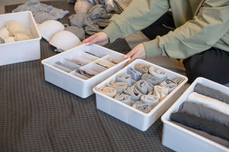 Young woman organizing underwear storage at bedroom. Contemporary folded container cases clothingの写真素材