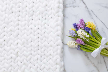 Bouquet of spring colored flowers of hyacinths. White marble background and fluffy knitted plaid