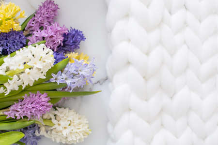 Bouquet of spring colored flowers of hyacinths. White marble background and fluffy knitted plaidの写真素材