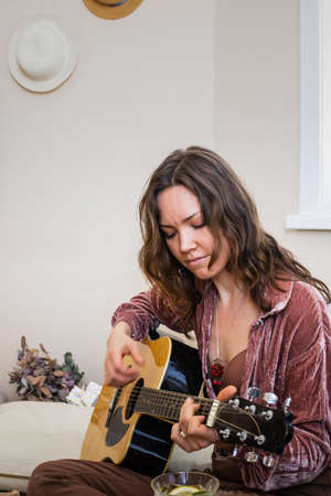Enthusiastic female playing guitar enjoying art hobby boho scandi home party singing song relaxing
