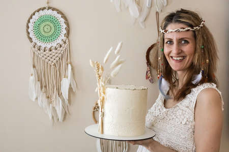 Happy elegant woman posing with tasty fresh cake cream beige decorated in boho scandi styleの写真素材