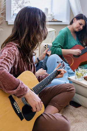 Group female friends playing guitar singing song having fun at hen-party in hippie bohemian style
