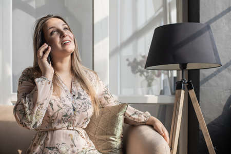 Young woman with long hair in in a beige nude business suit is talking on phone and writing notes