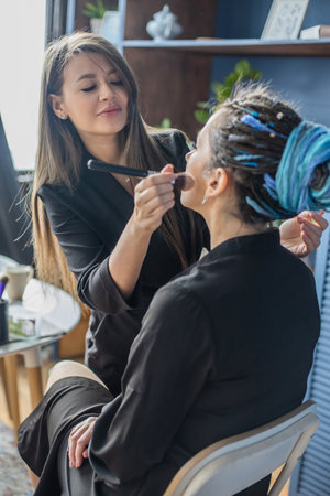 Hands of professional makeup artist applying eyeshadow concealer on eyes of female model use brushの写真素材