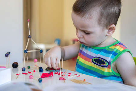 A little boy sculpts from plasticine at the table at home. Makes a tower of toothpicks and balls.の写真素材