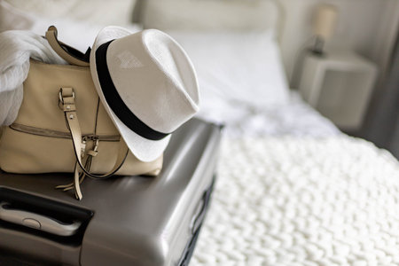 Gray suitcase with handbag and summer hat packing ready to travel vacation on bed at home or hotelの写真素材