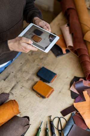 Top view male tanner use tablet at leather workshop. Craftsman creating online advertising promotionの写真素材