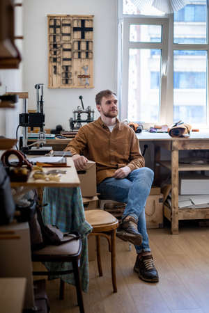 Smiling European male owner of small business posing at leather workshop. Professional tanner