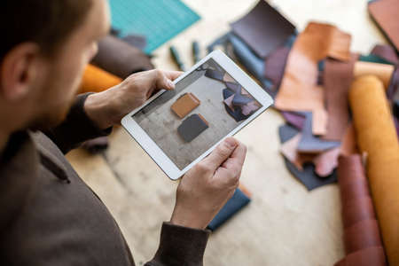 Top view male tanner use tablet at leather workshop. Craftsman creating online advertising promotionの写真素材