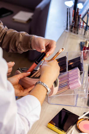 Female makeup artist parsing cosmetic bag of client. Teaching choosing brushes and lip glossの写真素材