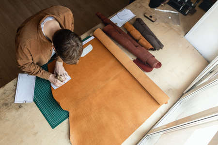 Male tanner making cutting scheme of bag working at leather workshop. Handcrafted creatingの写真素材