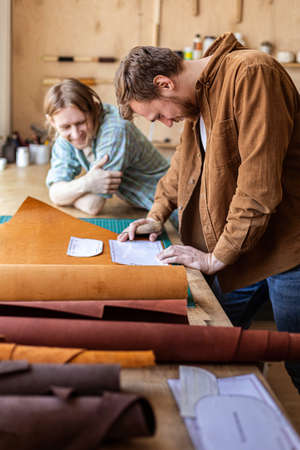 Craftsman unwrapping bundle of stuff natural material working at leather workshop. Leatherwork