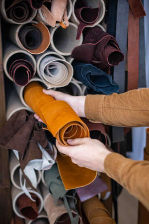 Closeup male craftsman taking material bundle for working at leather workshop. Making leathercraft