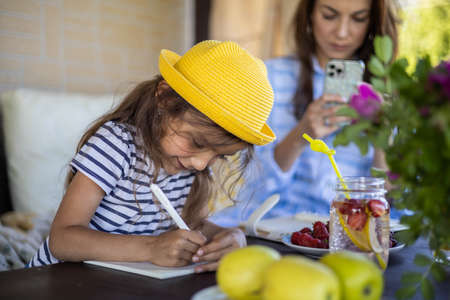 Focused mother and daughter looking paper schedule notebook together relaxing at outdoor terrace