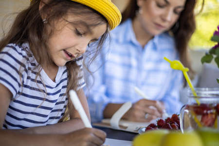Focused mother and daughter looking paper schedule notebook together relaxing at outdoor terrace