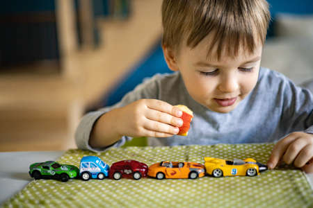 Little boy plays with toy cars while sitting at the table. Laughs and enjoys his toys.の写真素材
