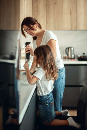 Mom and daughter prepare icing for gingerbread in their home kitchen. Beat with a blender. The girl helps the woman.の写真素材